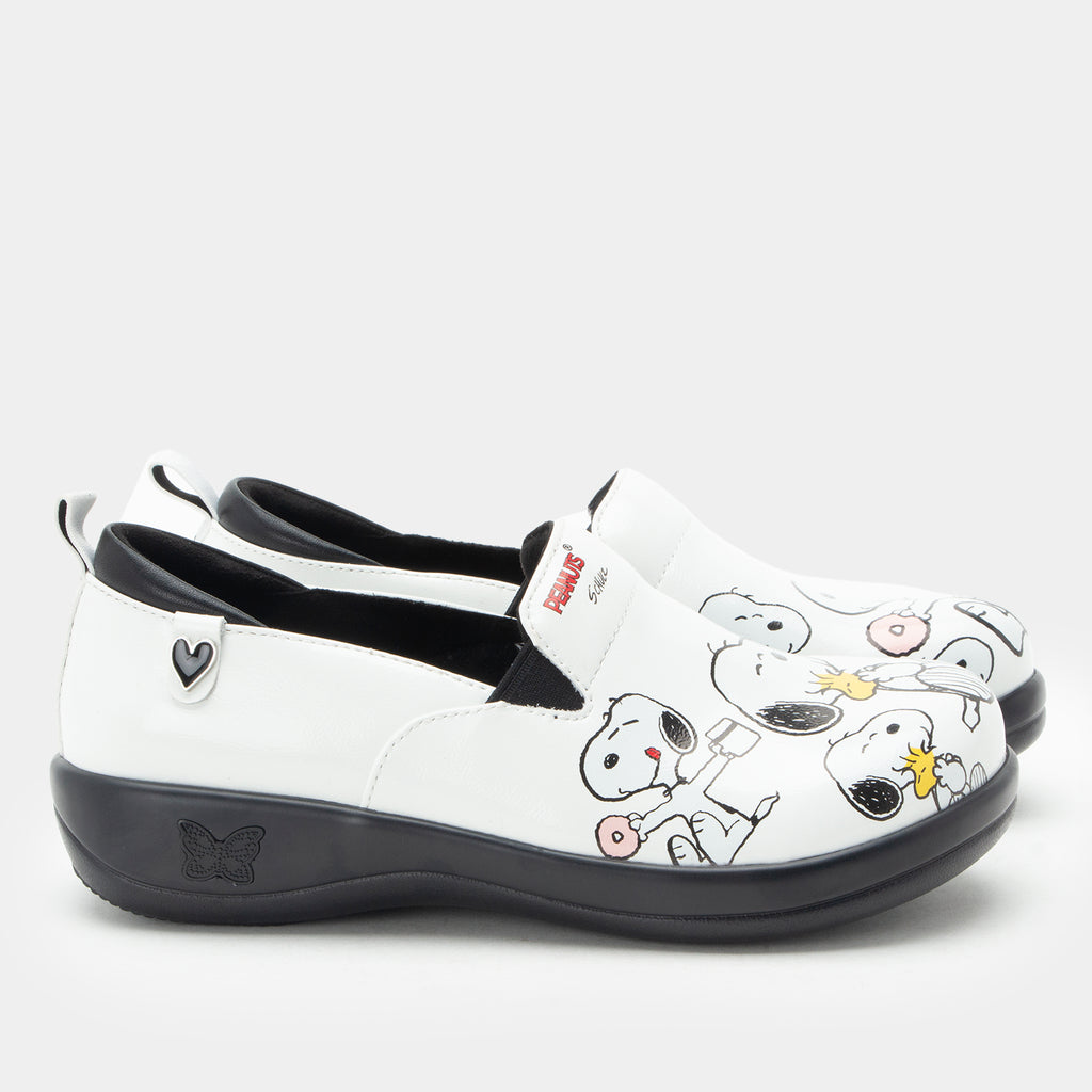 A pair of Alegria x Peanuts® white slip-on shoes featuring a black sole and cartoon Peanuts® characters print on the leather uppers. KEL-SNP19