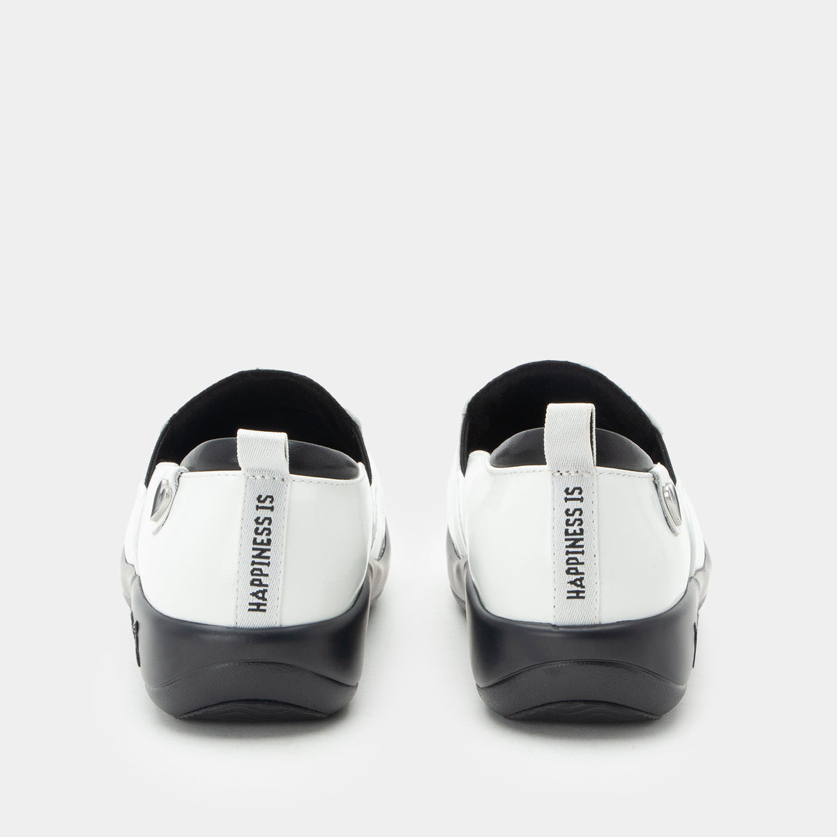 A pair of Alegria x Peanuts® white slip-on shoes featuring a black sole and cartoon Peanuts® characters print on the leather uppers shown from the back. The heel area features a white pull tab with the text 'HAPPINESS IS' printed vertically in black. KEL-SNP19