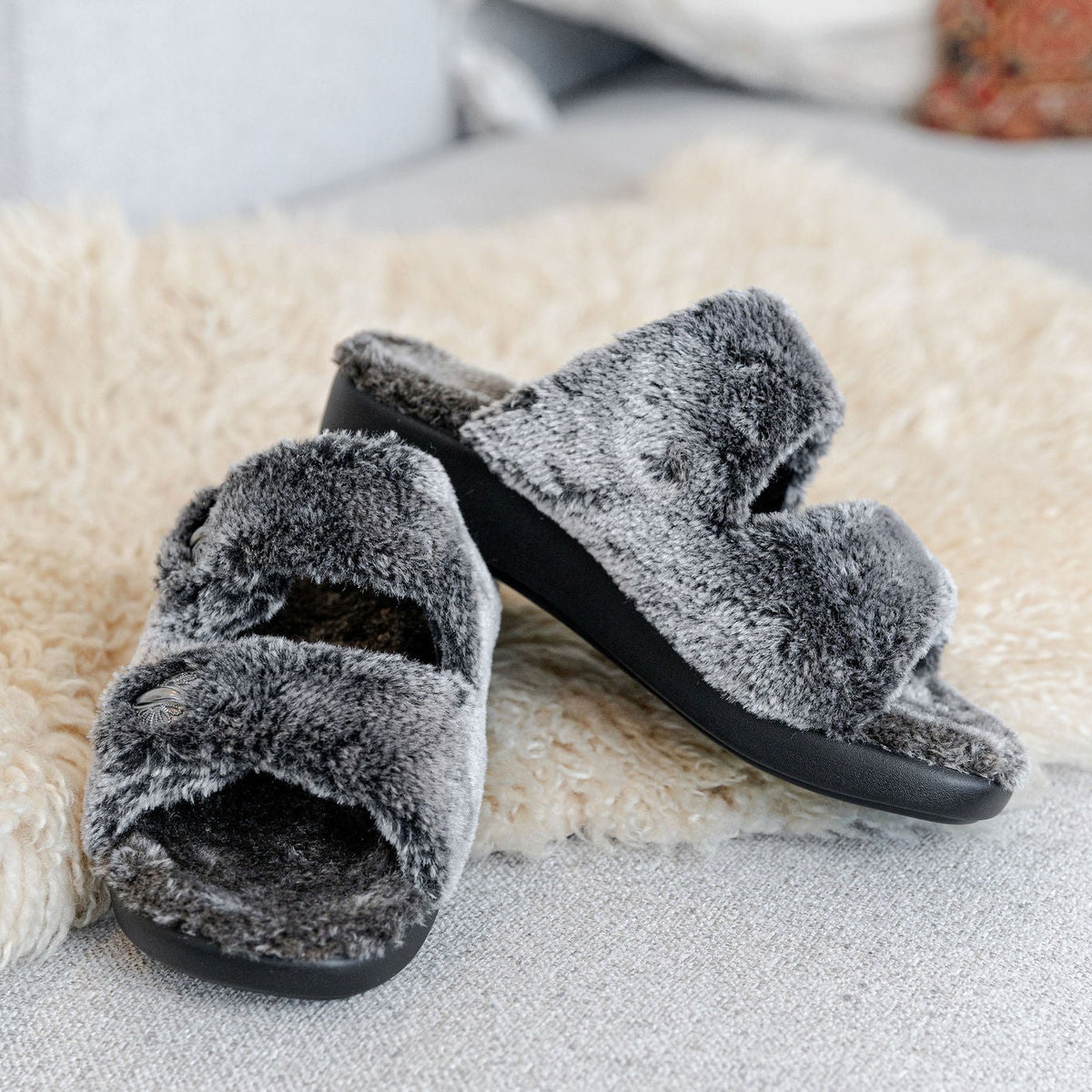 Pewter plush faux-fur double-strap Chillery slide slippers with black soles resting on a fleece mat.